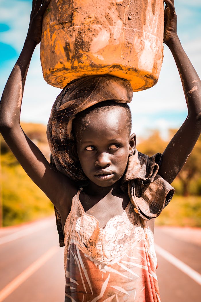 services-02 A young girl balances a water container on her head, walking on a road in rural Kenya.